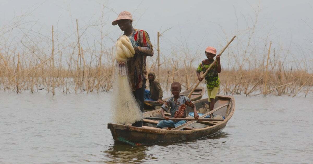 Ein Boot mit Vater und Sohn, der Vater hält ein Fischernetz in der Hand.