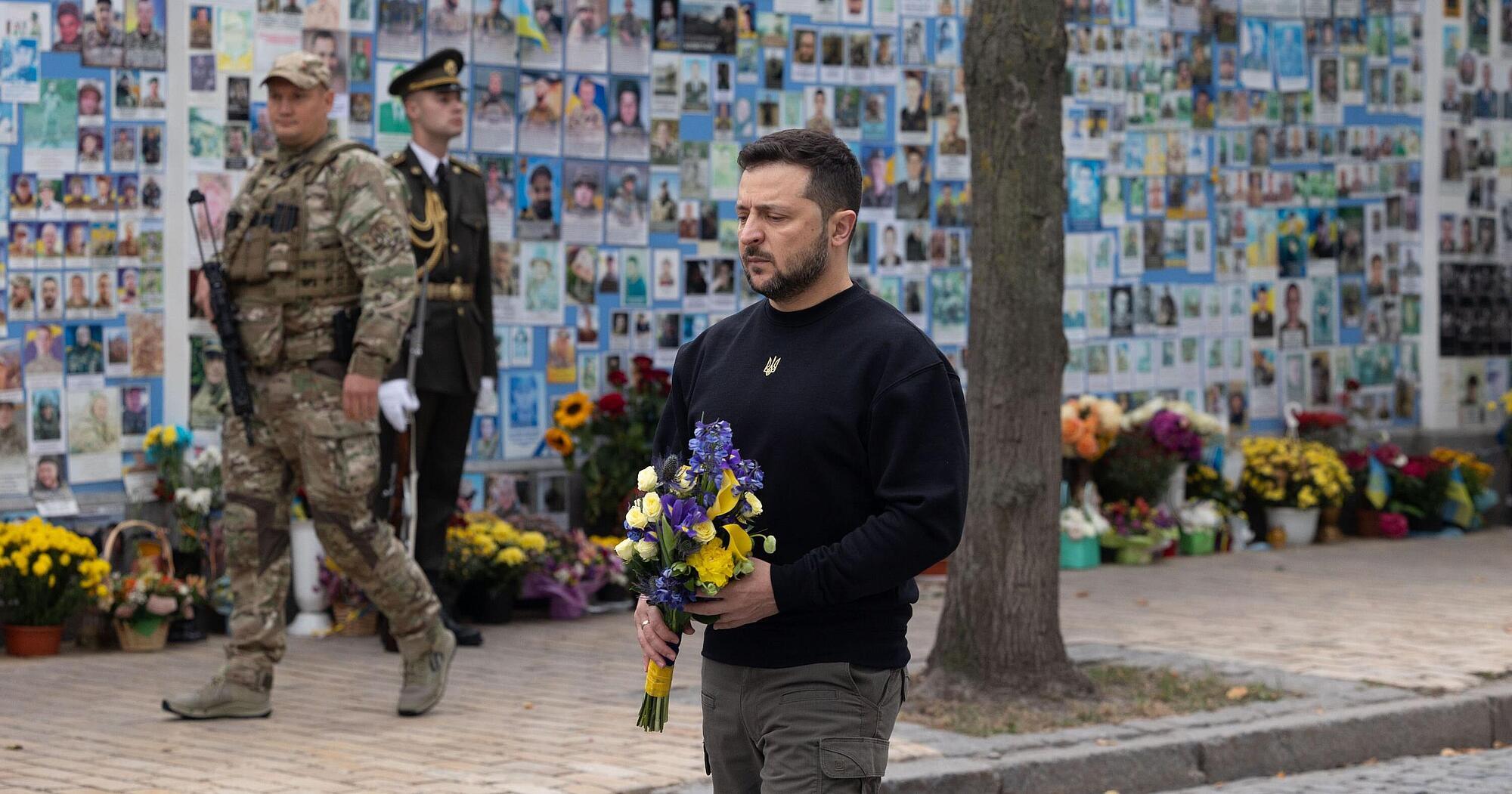 Ukraine President Selenskyj with flowers in his hands in front auf picture wall