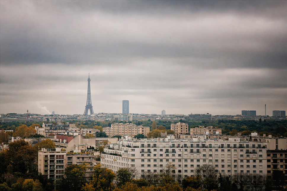 The Eiffel Tower rises majestically in the distance, framed by the sprawling urban landscape of Paris. Overcast skies lend a moody atmosphere to this stunning view, with glimpses of Puteaux hinting at the city's endless horizons.
