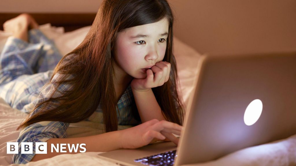 A young child looks curious as she uses a laptop.