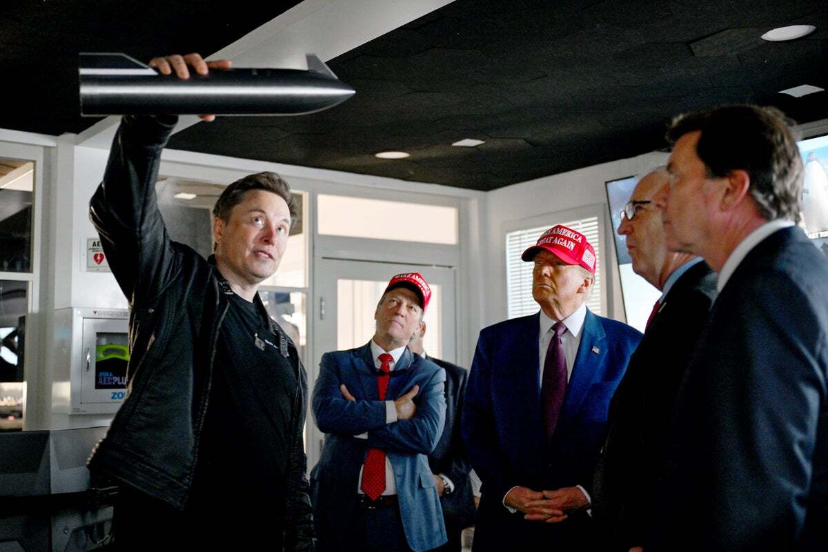 Elon Musk holds up a miniature model of SpaceX's Starship as Donald Trump and other visitors look on