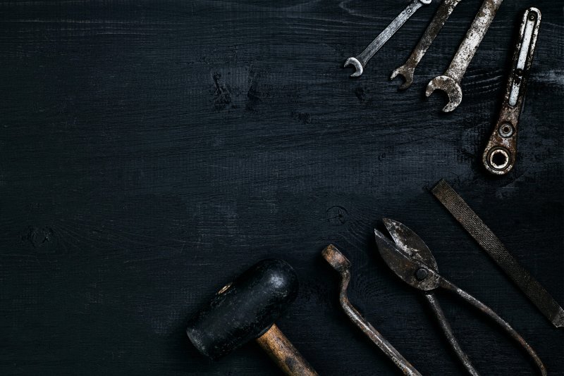 Alte, rostige Werkzeuge liegen auf einem schwarzen Holztisch. Hammer, Meißel, Metallschere, Schraubenschlüssel. Ansicht von oben.