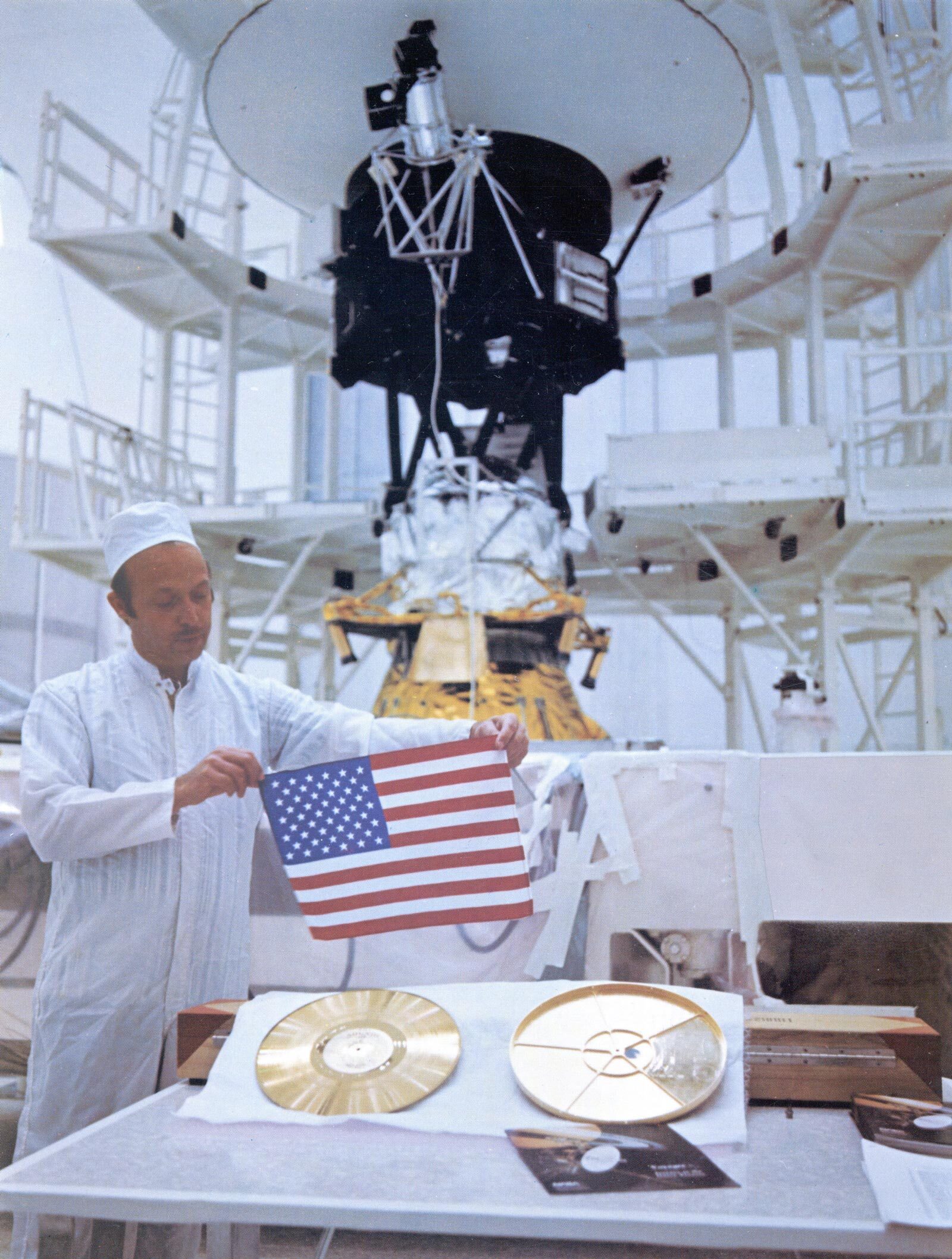 With Voyager 2 in the background, John Casani holds a small U.S. flag