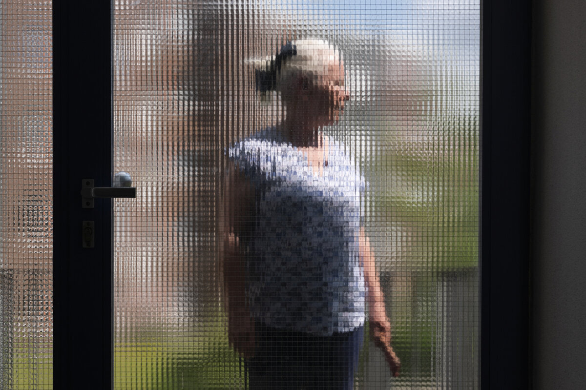 Eine Person ist anonymisiert hinter einer Scheibe fotografiert. Eine Person ist anonymisiert hinter einer Scheibe fotografiert.