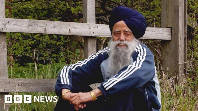 Fauja Singh rests after a run near his home in Ilford, England, Saturday, April 10, 2004. He's wearing a blue tracksuit and sitting with arms folded, smiling at the cameras.