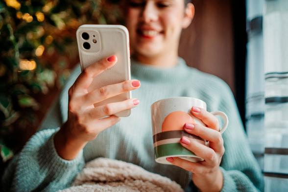 Young caucasian woman use phone send sms text messages and drink coffee by the window Young caucasian woman use phone send sms text messages and drink coffee by the window