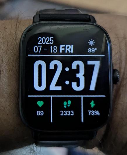 A smartwatch with the a plain black background and an off white display. The time is HUGE so it is very visible. The date is at the upper left in smaller font  and the temperature is visible in smaller font to the right. At the bottom in a similar font to the temperature are heart rate (89) , steps walked ( 2333 need to walk some more !! )  and the battery charge 73%