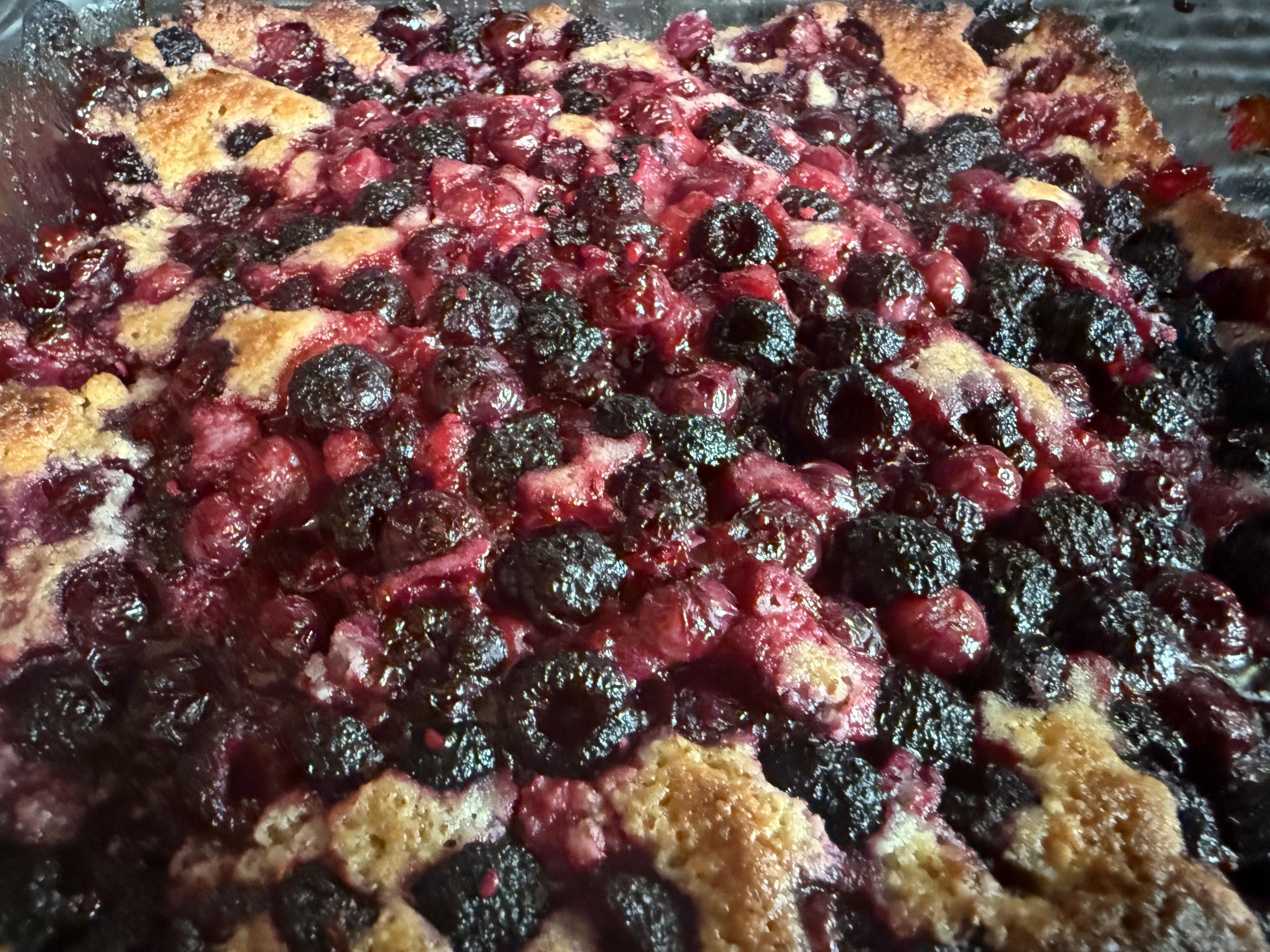 low and closeup to a very berry ladened cake. Bits of brown cake are poking up here and there, but mostly berries, berries, berries.