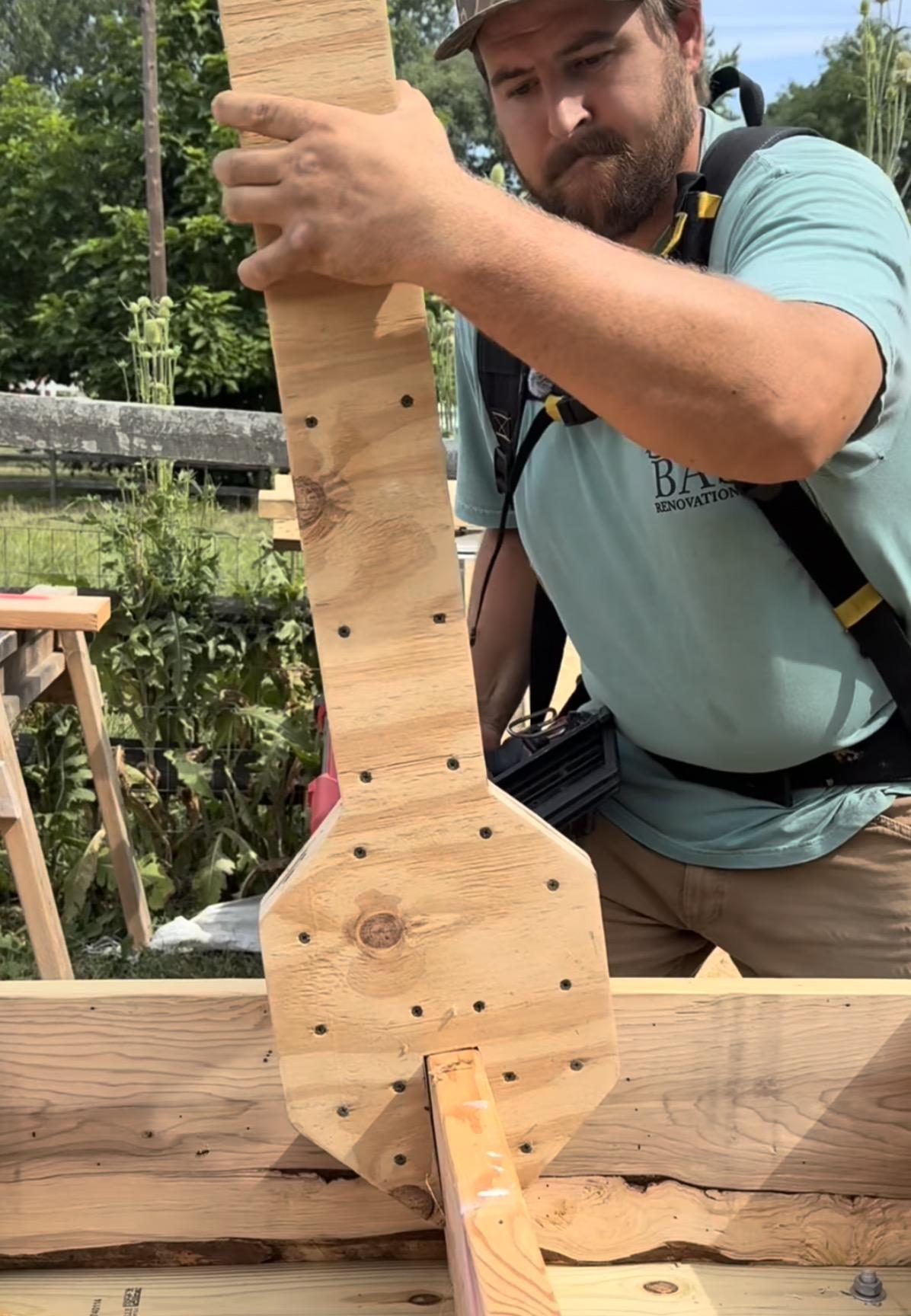 Man holding a comically giant wooden wrench to straighten a joist before nailing it in place.