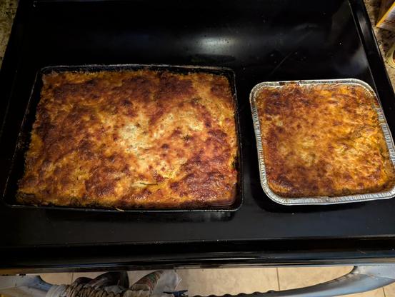 Two pans of lasagna sitting on a black glass stove top.The larger is in a regular black aluminum pan that has 3 layers. The smaller is in a disposable aluminum pan that has been used a few times so is slightly crinkled.

The larger pan has 3 layers consisting of homemade meat sauce, zucchini, a mix of ricotta, cottage cheese,Parmesan  and parsley and then a layer of mozzarella repeated 3 times. The smaller 2 layers of the same combination .

Since I like it with the cheese surface almost burnt …