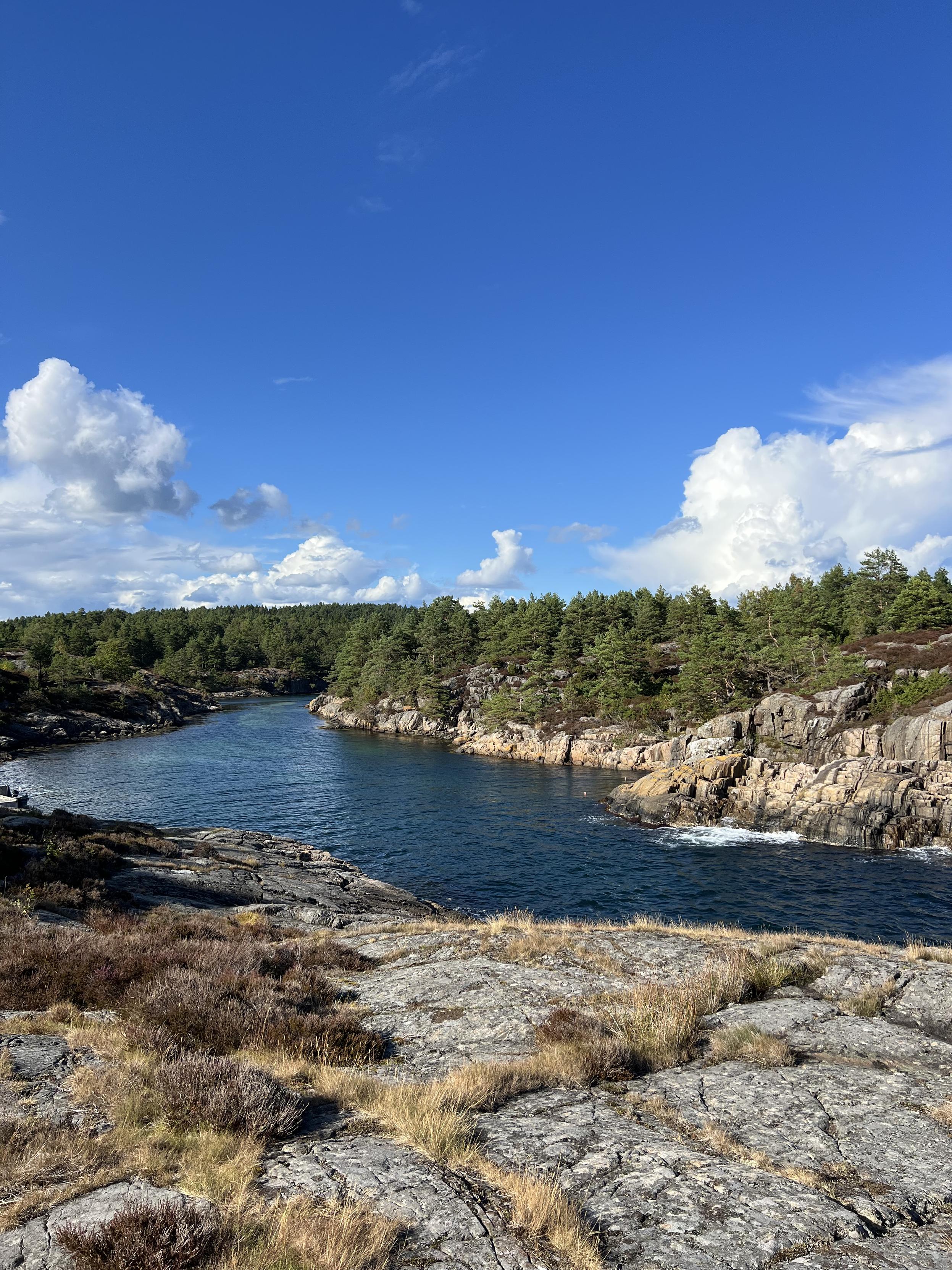 A photo taken on a sunny day in southern Norway, showing a coastal scene with rocks and the ocean on the island of Flostaøya.